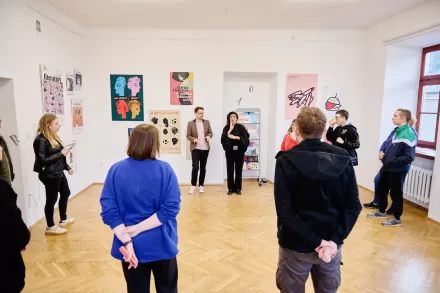 Grupa ludzi słucha przemowy na wernisażu.