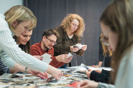Grupa kobiet siedzi dookoła stołu i ogląda zdjęcia, które leżą na blacie.