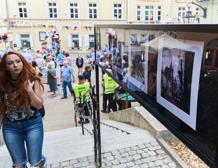 Tłum ludzi na ulicy. Kobieta podchodzi do gabloty i przygląda się jej.