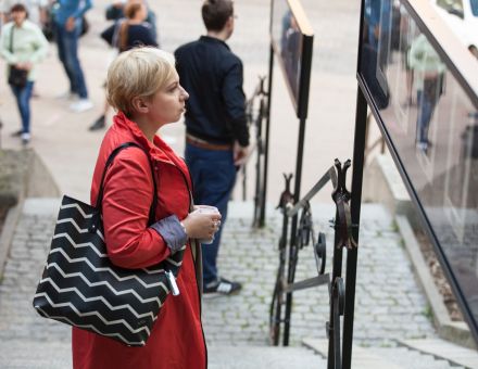 Plenerowa wystawa w Zaułku Hartwigów, zbliżenie na kobietę podziwiającą zdjęcia. Michała Greima