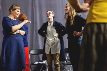 Na zdjęciu prowadząca pokazuje jednej z uczestniczek żeby obniżyła swój głos. Ta się śmieje.