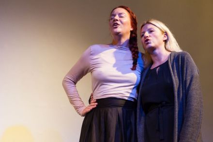 Zdjęcie przedstawia dwie kobiety podczas występu na scenie.