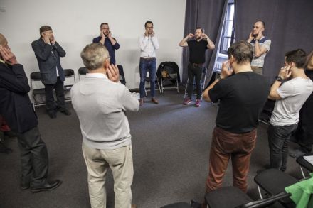 Na zdjęciu wszyscy uczestnicy powtarzają ćwiczenia jakie proponuje prowadzący. Trzymają dłonie blisko uszu.