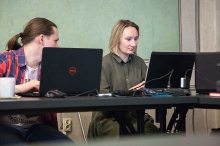 Widok na biurko, przy którym siedzą uczestnicy szkolenia. Młoda kobieta i mężczyzna patrzą w ekrany laptopów. Mężczyzna zwraca się w stronę kobiety, konsultują się.