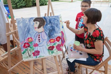 Zdjęcie ukazuje chłopca, który przygląda się kobiecie, kiedy ta maluje jego sylwetkę.