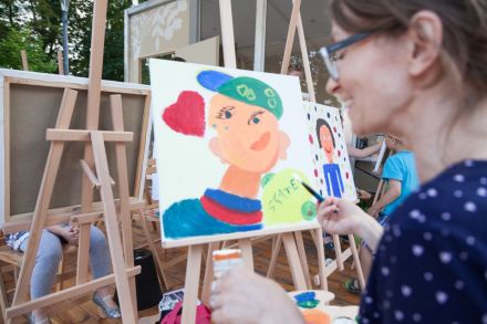 Na zdjęciu widać kobietę, która kończy malować swój obraz, przedstawiający chłopcy lubiącego styl hiphopowy.