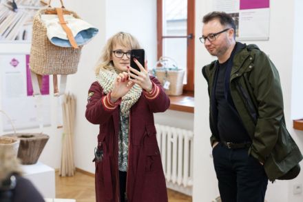 Zmiana otoczenia. Uczestnicy szkolenia w sali wystawowej Warsztatów Kultury. Rozpoczęcie części warsztatowej szkolenia. Jedna z uczestniczek trzyma w wyciągniętej ręce telefon, prawdopodobnie robi zdjęcie lub nagrywa film. Drugi z uczestników szkolenia przygląda się jej temu z zainteresowaniem.