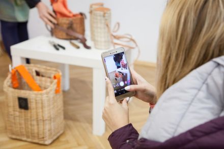 Część warsztatowa szkolenia - uczestnicy tworzą Instastories w sali wystawowej Warsztatów Kultury. Wystawa przedstawia wyroby plecionkarskie. Zbliżenie na telefon osoby robiącej Instastories.