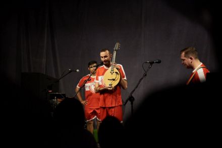Stojący na scenie muzyk pokazuje instrument strunowy. Jest to banjo.