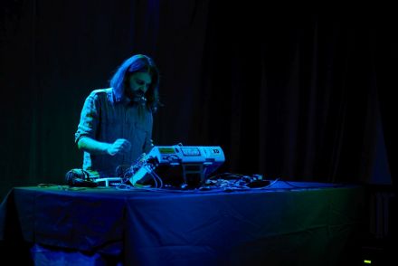 Zdjęcie ukazuje  artystę, który stoi na przeciwko miksera do miksowania dźwięków.