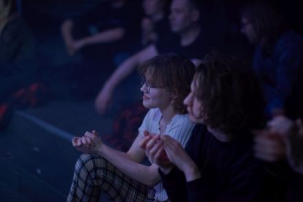 Zbliżenie na osoby siedzące na widowni. Wszyscy patrzą w scenę.