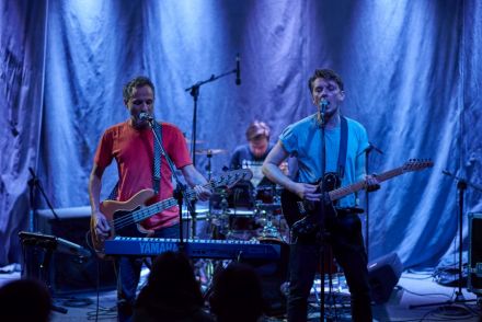 Widok z naprzeciwka na cały zespół stojący na scenie. Zespół w składzie Artur Soszyński, Łukasz Płata i Karol Morawski.