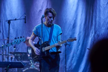 Na zdjęciu dominuje kolor niebieski, zdjęcie przedstawia gitarzystę w trakcie grania na gitarze.