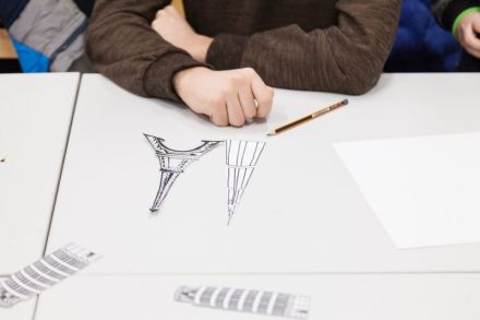 Warsztat architektoniczny  [warsztat dla dzieci w ramach Zimowej Majsterni. Na zdjęciu widzimy szkice budynków, dziecięce dłonie oraz leżący obok ołówek i czystą kartkę papieru]