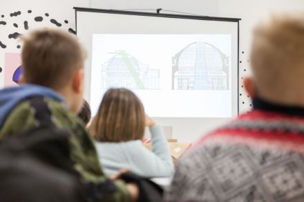 Warsztat architektoniczny [warsztat dla dzieci w ramach Zimowej Majsterni. Na zdjęciu dzieci przyglądają się wyświetlonym z rzutnika przykładowym budynkom]