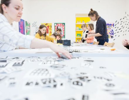 Na zdjęciu dzieci siedzące przy stole, na którym znajduje się mnóstwo kartek.