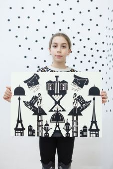 Na zdjęciu stoi kolejna dziewczynka, trzymająca plakat utrzymany w kolorystyce biało-czarnej. Widzimy kilka budynków, tworzących abstrakcyjny obraz. Są one zawieszone w przestrzeni. Pomiędzy dwoma budynkami znajduje się napis "latający sklep".