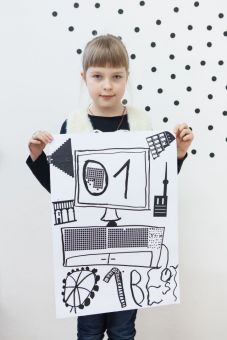 Na zdjęciu stoi dziewczynka trzymająca plakat utrzymany w kolorystyce biało-czarnej. Widzimy wielki ekran na środku plakatu oraz malutkie budynki dookoła.