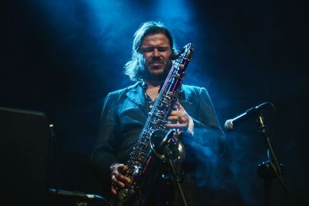 Zbliżenie na saksofonistę. Ma zamknięte oczy. Trzyma w rękach instrument, ale na nim nie gra. Wokół niebieski dym.