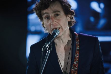 Wokalista, bliski kadr, mężczyzna patrzy prosto w obiektyw. Śpiewa do mikrofonu.