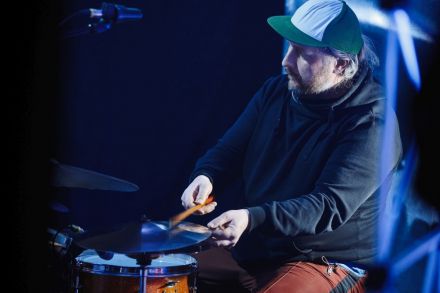 Zbliżenie na perkusistę w czapce. W rękach trzyma pałeczki.