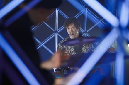 DJ patrzy prosto w obiektyw. Widać go zza kratownic i perkusji. Nie uśmiecha się, jest bardzo poważny.