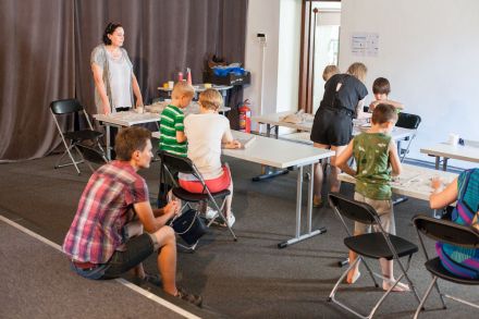 Dzieci i rodzice siedzą przy stolikach i robią płaskorzeźby z gliny.