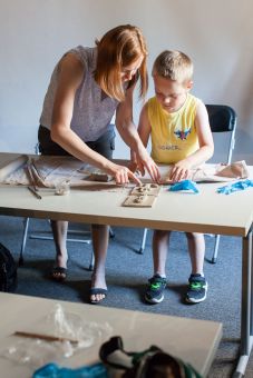 Kobieta i chłopiec stoją nad dwiema płaskorzeźbami, które leżą na stole.