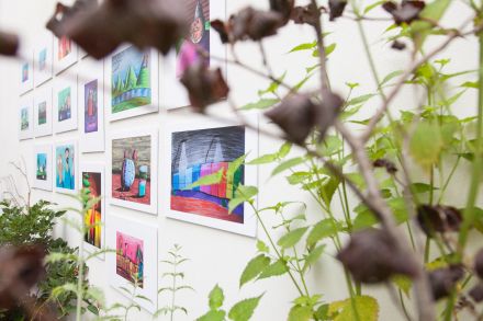 Obrazy na wystawie przesłonięte bluszczem i kwiatami.