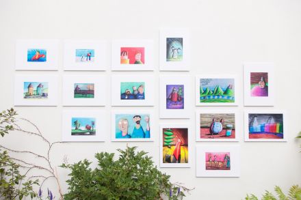 Zbliżenie na jedną ścianę z obrazami z wystawy. Poniżej kwiaty.