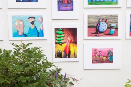 Zbliżenie na cztery obrazy z wystawy. Przedstawiają kolejno: trzech mężczyzn, chłopca z prezentem pod choinką, budzik i szklankę wody oraz czworo ludzi i kota.