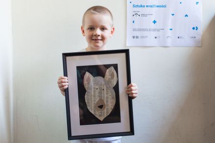 Chłopiec trzyma w ręce gotowy obrazek - psa z gazety. Jest uśmiechnięty i dumny z efektu.