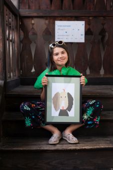 Dziewczynka siedzi na drewnianym podeście i prezentuje swoją gotową pracę.