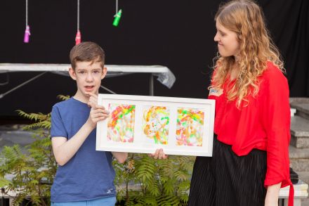Chłopiec wraz z prowadzącą warsztaty trzyma efekt końcowy swojej pracy - obraz powstały z mazajów farbami.