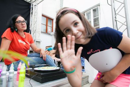 Dziewczynka biorąca udział w warsztatach uśmiecha się do obiektywu i macha w jego stronę.