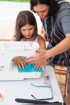 Prowadząca warsztaty pokazuje dziewczynie, jak należy szyć na maszynie.