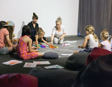 Dzieci siedzą w kręgu i wyklejają obrazek z bibuły.