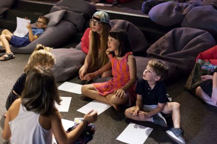 Dzieci siedzą na podłodzie. Przed nimi leżą kartki.