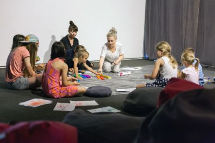 Dzieci siedzą w kręgu i wyklejają obrazek z bibuły.