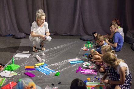 Dzieci wraz z prowadzącą siedzą na podłodze i wyklejają obrazek z bibuły.