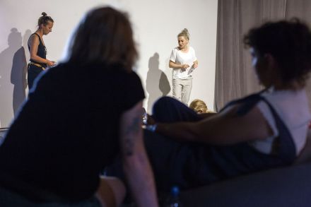 Dwie prowadzące stoją i opowiadają. Dzieci z rodzicami siedzą i słuchają.