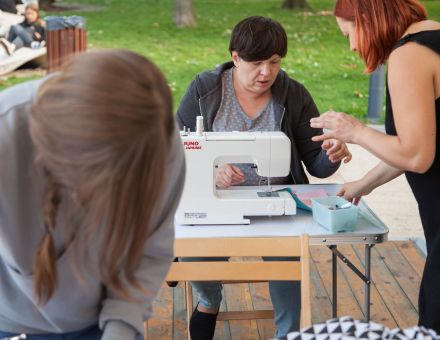 Prowadząca pokazuje kobiecie, jak zszyć materiał.