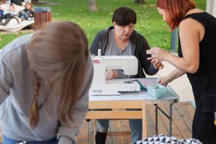 Prowadząca pokazuje kobiecie, jak zszyć materiał.