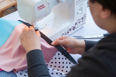 Zbliżenie na dłonie kobiety, która zszywa ścieżkę sensoryczną na maszynie.