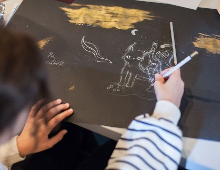 Zbliżenie na dłoń dziewczynki i kartkę, na której rysuje obrazek.