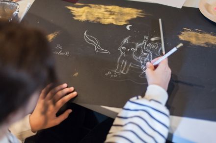 Zbliżenie na dłoń dziewczynki i kartkę, na której rysuje obrazek.