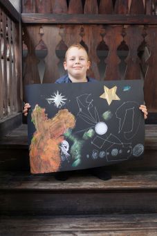 Chłopiec siedzi na schodach i prezentuje gotowy obrazek.