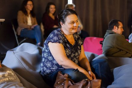 Zbliżenie na kobietę siedzącą na publiczności. Uśmiecha się.