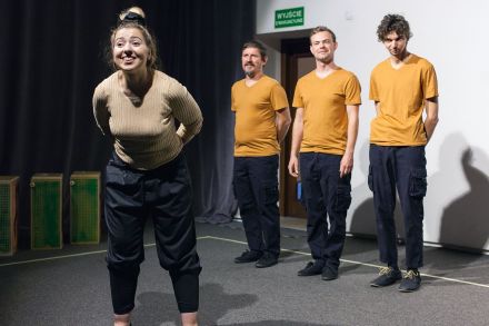 Trzej aktorzy w żółtych koszulkach i kobieta, która stoi przed nimi i kłania się publiczności.