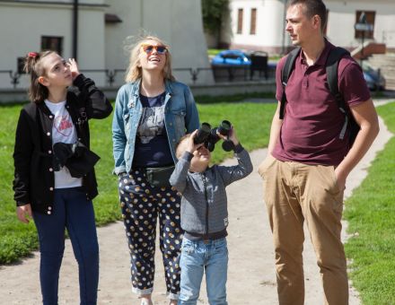 Rodzina uczestnicząca w spacerze. Chłopiec patrzy przez lornetkę w niebo.